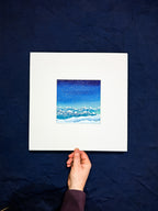 Hand holding a framed artwork of a night sky with clouds against a dark blue background