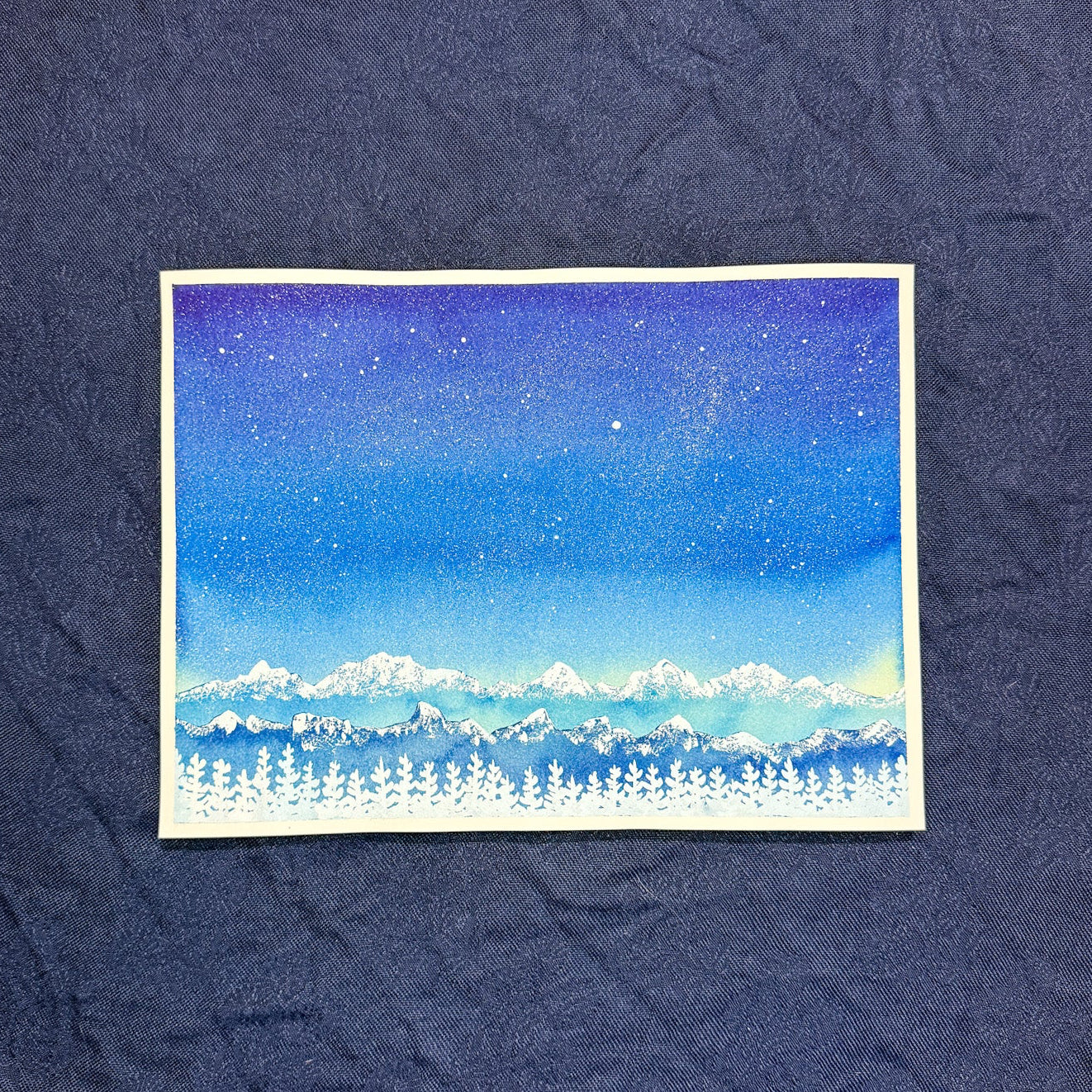 Small painting of a snowy landscape with mountains on a textured blue background
