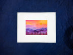 Framed artwork of a sunset over mountains and trees on a textured blue background