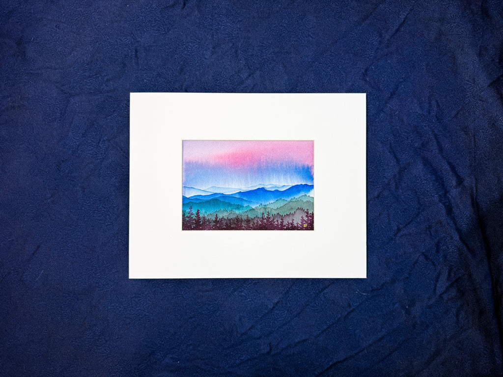 Small painting of a mountain landscape watercolor painting in a white mat on a textured blue fabric background