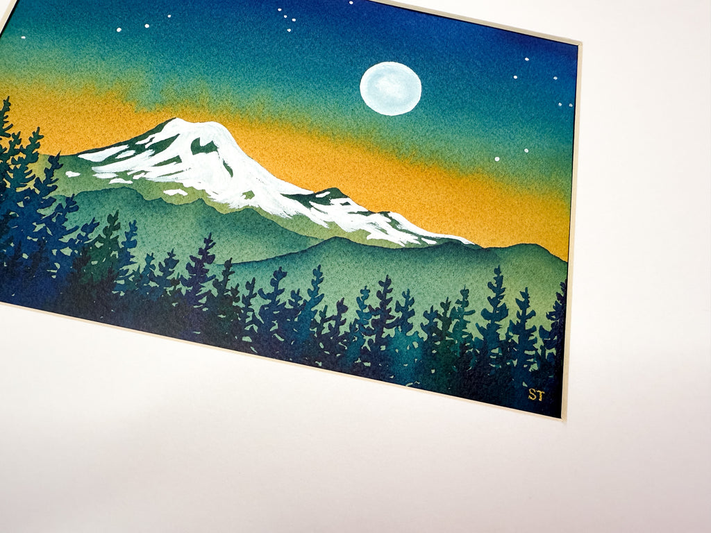 Framed artwork of a mountain landscape watercolor painting with trees and a moonlit sky.