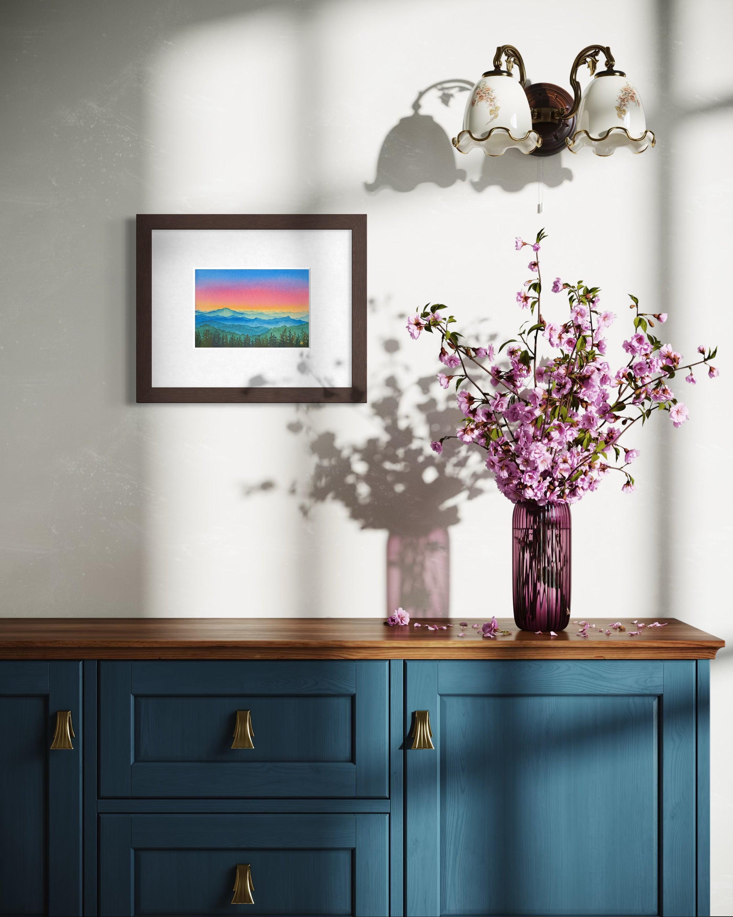 Blue cabinet with a wooden top featuring a vase of pink flowers and a framed picture on a white wall.